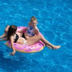 mom and daughter swimming in an above ground pool in a pink frosted donut pool float